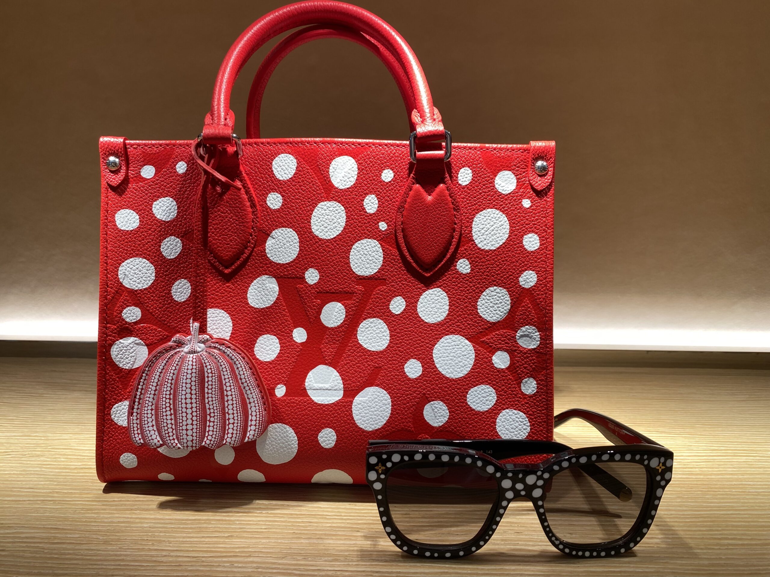 Red purse with polka dots on a table. Sunglasses with polka dots are sitting in front.